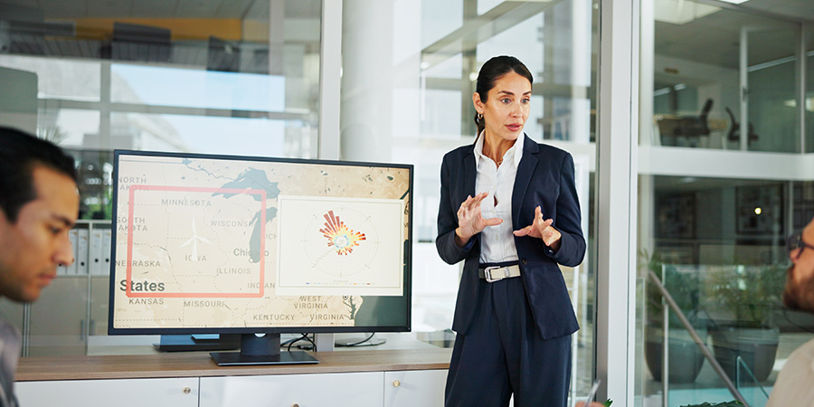 An emergency management specialist leads a meeting in front of a monitor showing a regional map. 