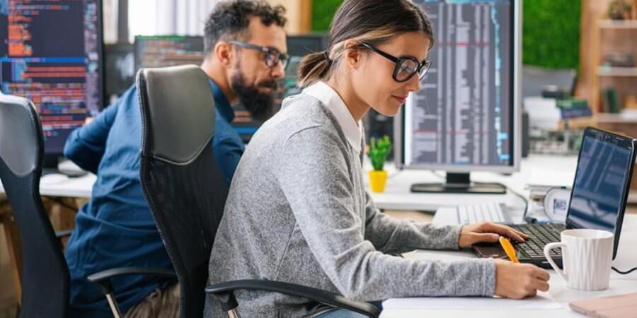 Two data scientists work on computers with monitors displaying code beside them.